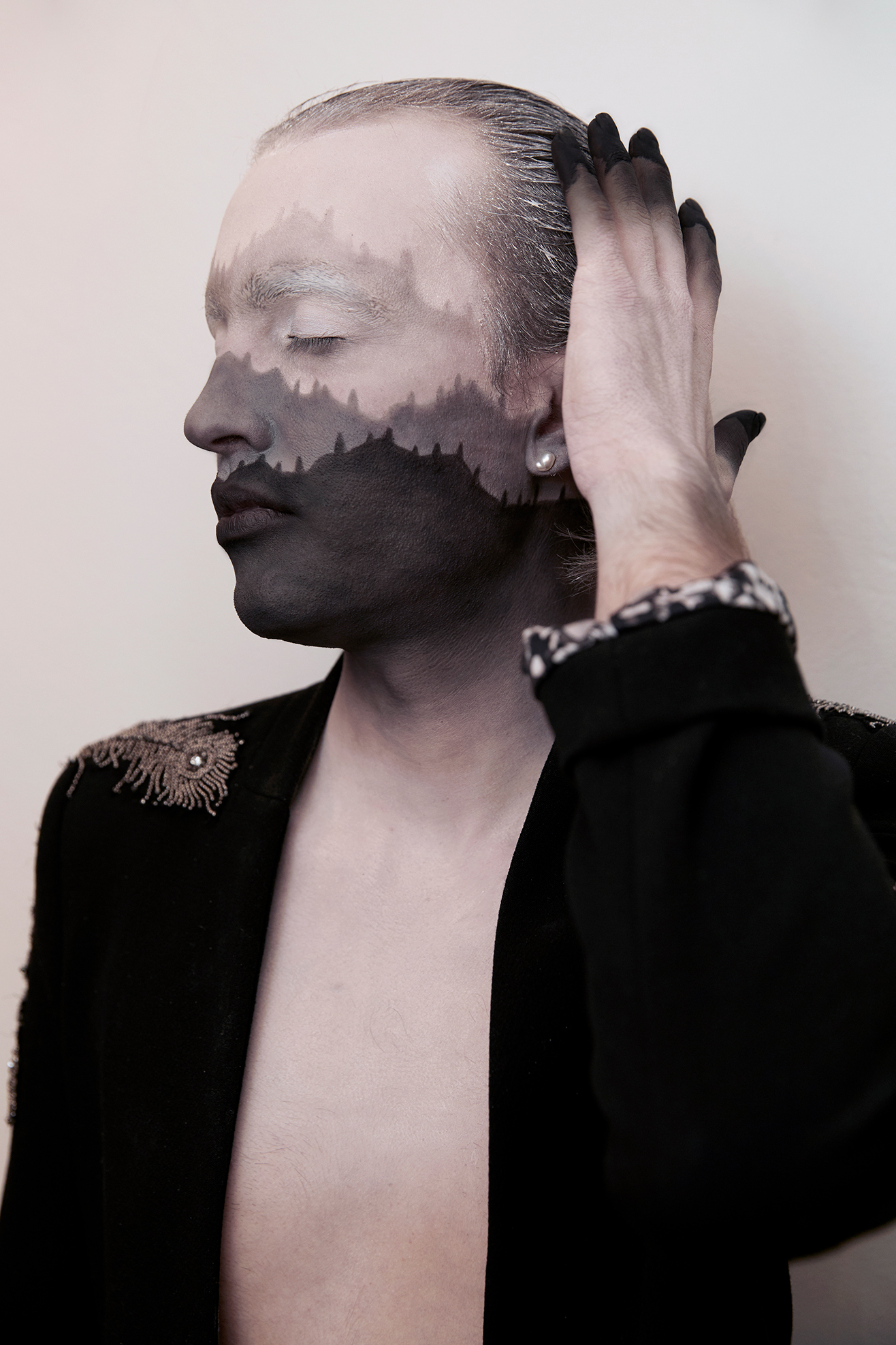 Jesse Clark posing his hand on one side of his head with black and white facepaint that resembles a mountain range against a white background
